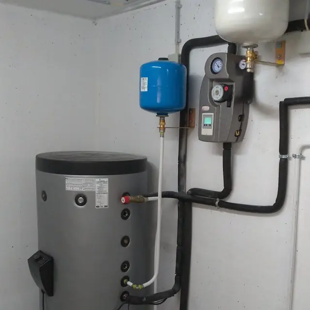 Depósito de água quente numa garagem, com central solar de bombagem na parede e dois vasos de expansão.