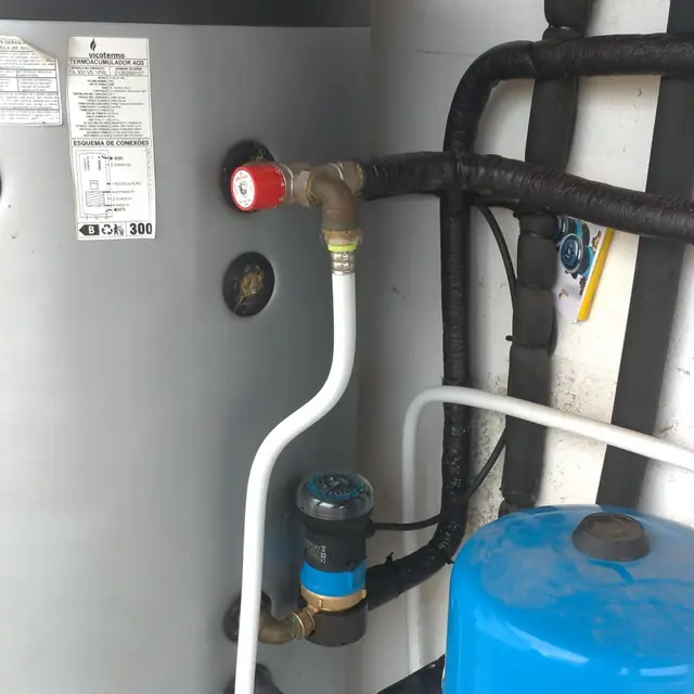 Depósito de água quente de 300 litros com tubagem branca e preta, válvulas e um vaso de expansão azul.