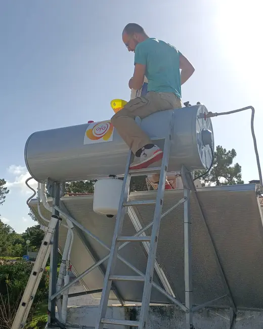 Técnico sentado no depósito de um termossifão, no telhado, a fazer a manutenção.