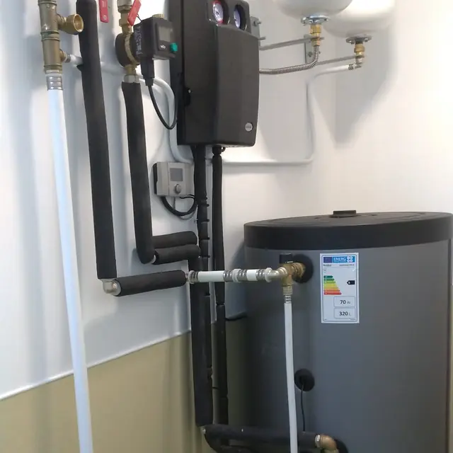 Depósito de água quente com central solar e tubagem isolada numa sala técnica.