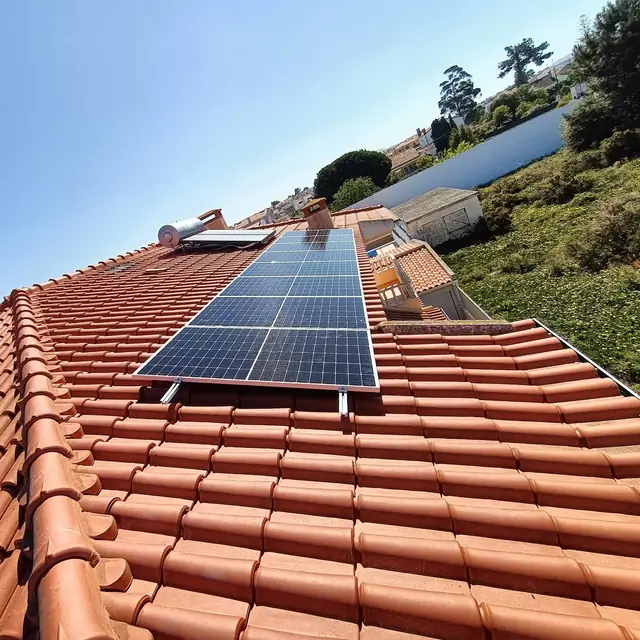 Telhado de telha visto de baixo, com uma fila de painéis fotovoltaicos e um termossifão ao fundo.