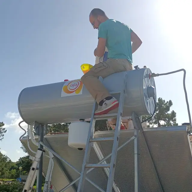Técnico sentado no depósito de um termossifão, no telhado, a fazer a manutenção.